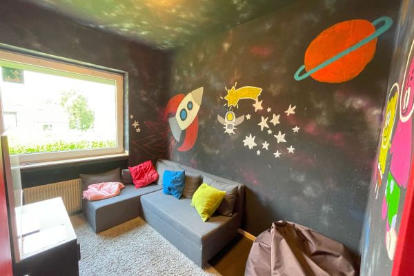 Jugendraum mit bunten Wänden, einem Sofa mit buntem Kissen drauf.
