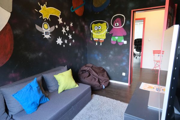 Raum mit bunt angemalten Wänden, einem Sofa und einer Playstation samt Bildschirm.