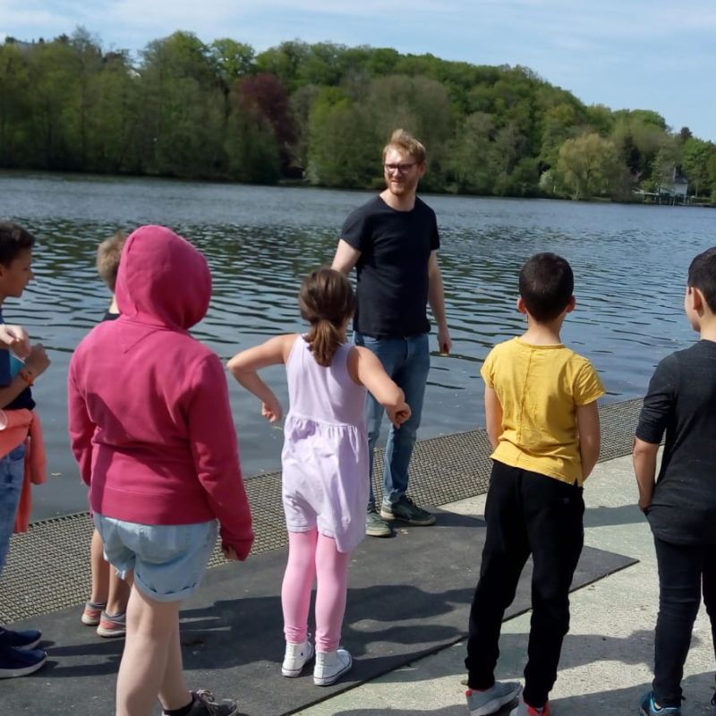 Kinder stehen am Ufer des Baldeneysees und werden für eine bevorstehende Kanufahrt angeleitet.