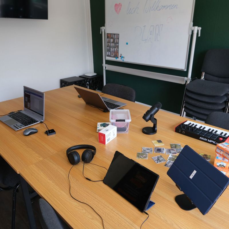 Medienraum mit Tischen, auf denen verschiedene Endgeräte stehen: Mikrofon, Tablets, Keyboards, Makey Makey, Kopfhörer und Laptops.