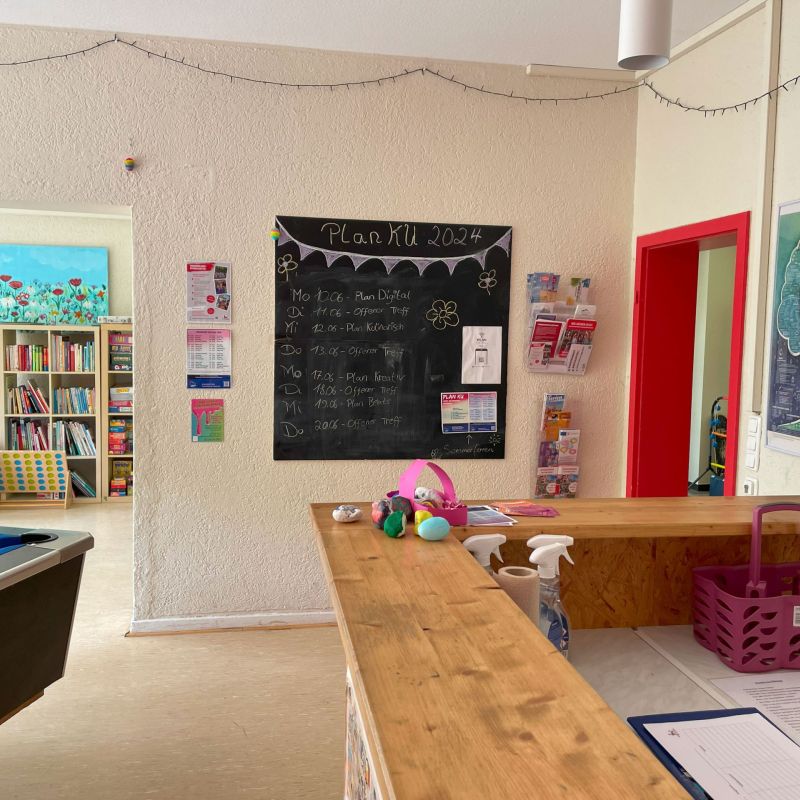Heller freundlicher Raum mit bunten Bildern, Kreidetafel mit Tagesprogramm, Theke, Billiardtisch und Bücherregal.