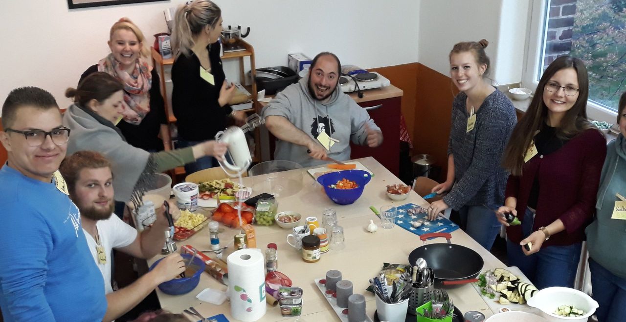 Jugen Menschen sitzen um einen gedeckten Tisch herum und essen gemeinsam ihr im Kochworkshop gekochtes Essen.