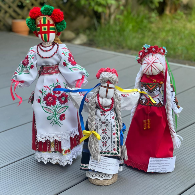 Drei Figuren die handgefertigt sind mit bunten Kleidern und geflochteten Zöpfen.