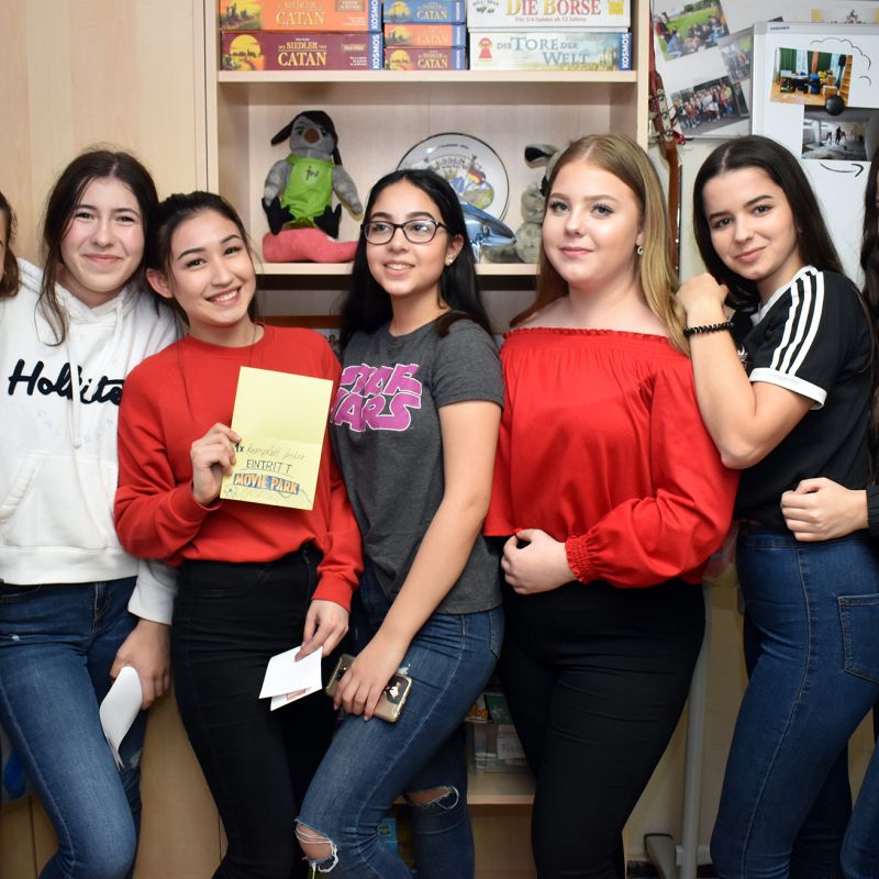 Sieben Mädchen im Kinder- und Jugendclub H21 Zero machen ein Gruppenfoto miteinander und lächeln in die Kamera.