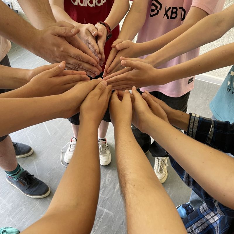 Ausgestreckte Arme mit zusammengefaltenen Händen verschiedener jungen Menschen, die alle zusammen einen Stern aus Armen bilden.
