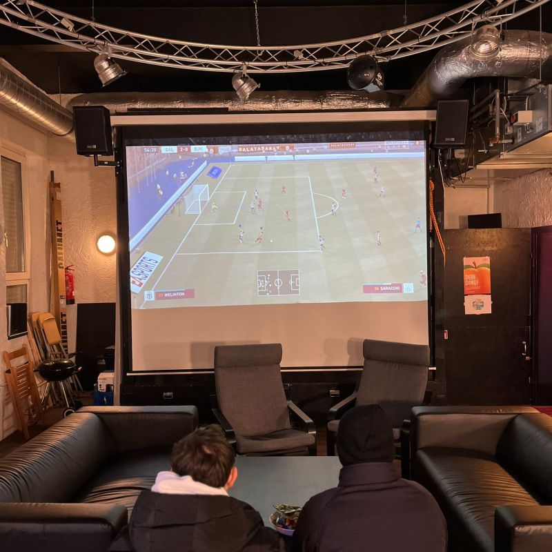 Zwei Jugendliche spielen im Jugendclub zusammen Fifa auf einer großen Leinwand.