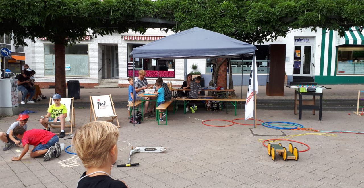 Auf dem Kupferdreher Marktplatz hat das Jugendwerk Essen einen Pavillon aufgebaut, Outdoorspiele mitgebracht und Liegestühle. Verteilt auf dem Platz spielen Kinder und nutzen das mobile Angebot.