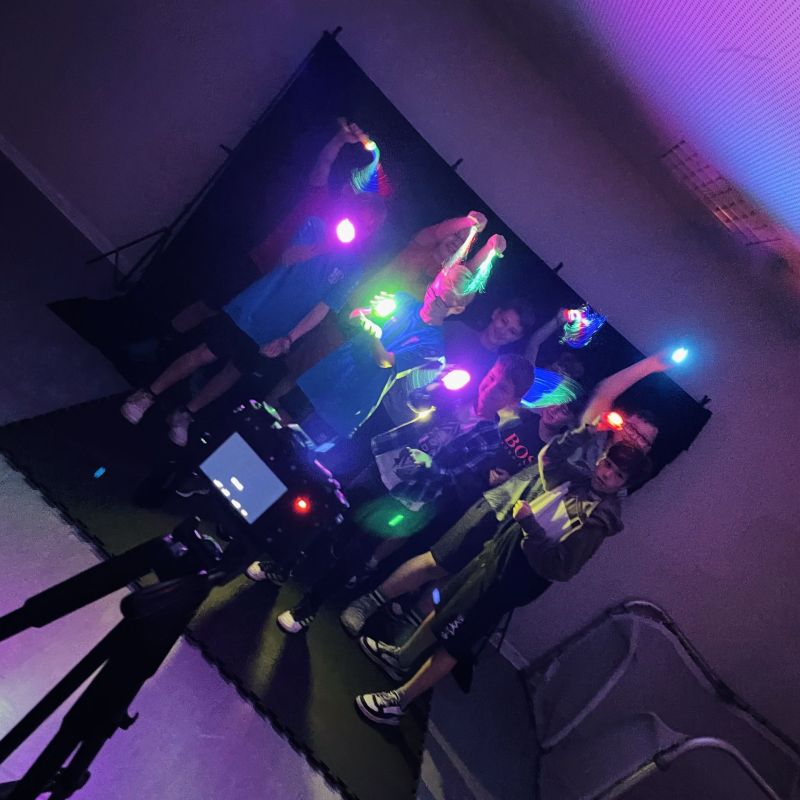Gruppe junger Leute testet Lightpainting. Im Vordergund ist eine Kamera zu sehen, im Hintergrund die Kinder mit bunten Lampen.