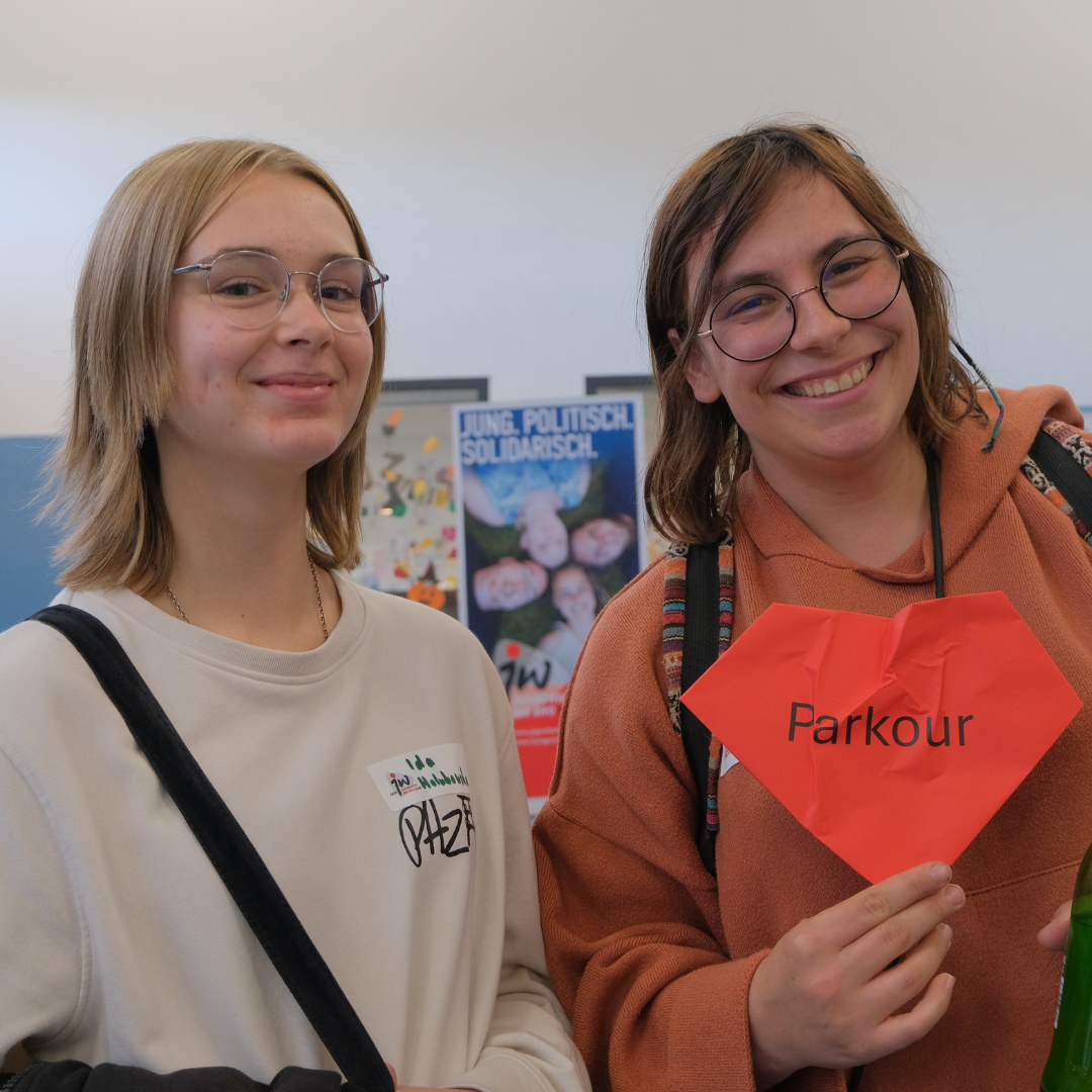 Zwei Besucherinnen lächeln in die Kamera und halten ein rotes Herz hoch auf dem 'Parkour' steht.