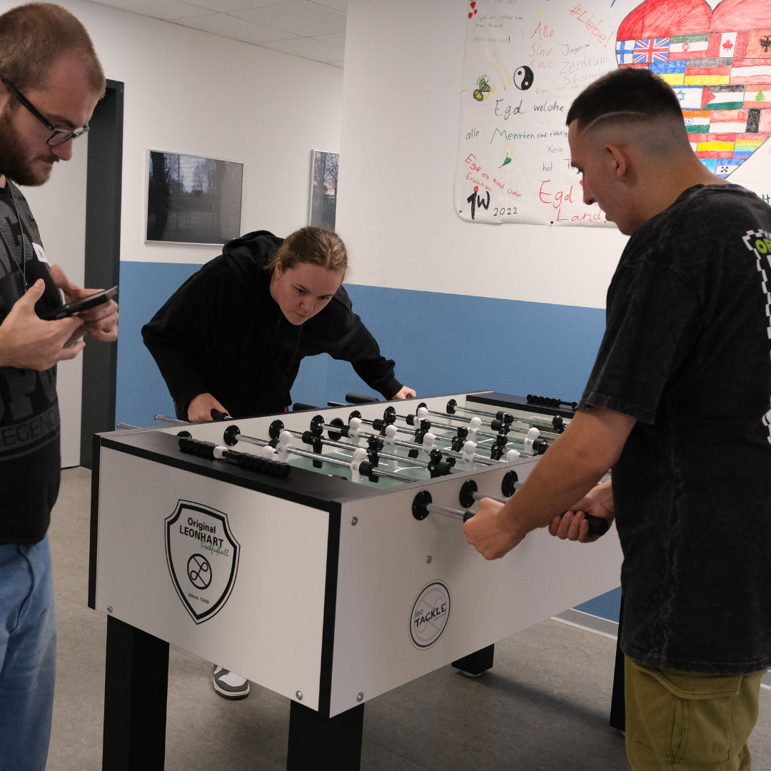 Drei Besuchende der Kreiskonferenz spielen gemeinsam Tischkicker.