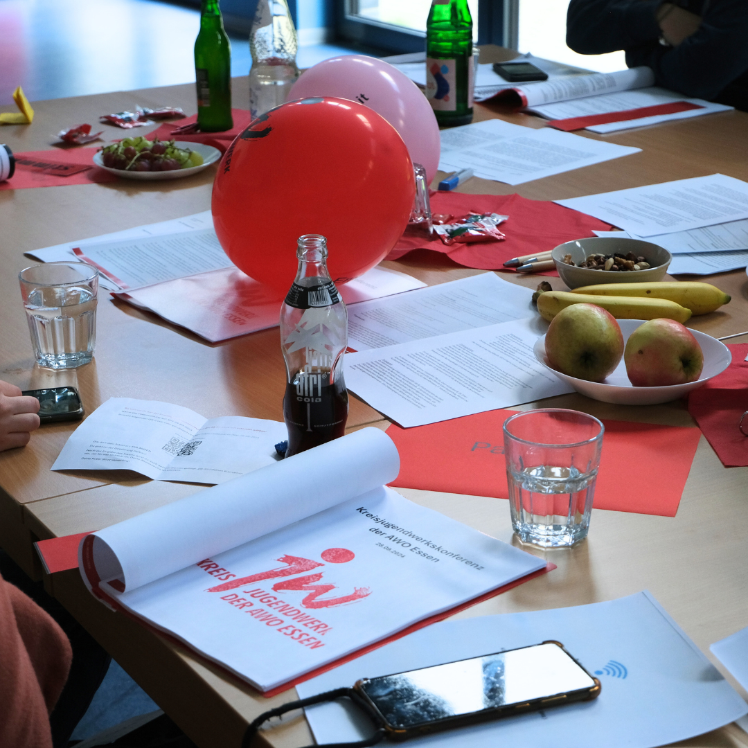 Detailaufnahme der Tische auf der Konferenz. Zu sehen sind die Konferenzmappe, Luftballons und Verpflegung.