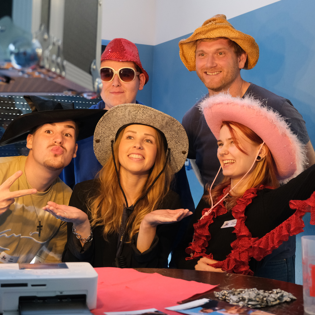 Besuchende der Konferenz haben sich verkleidet und lächeln in eine Fotobox um gemeinsam ein Bild zu machen.